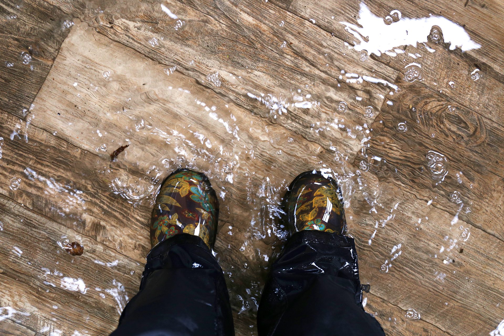 A person standing on a wooden floor in a pair of rain boots.