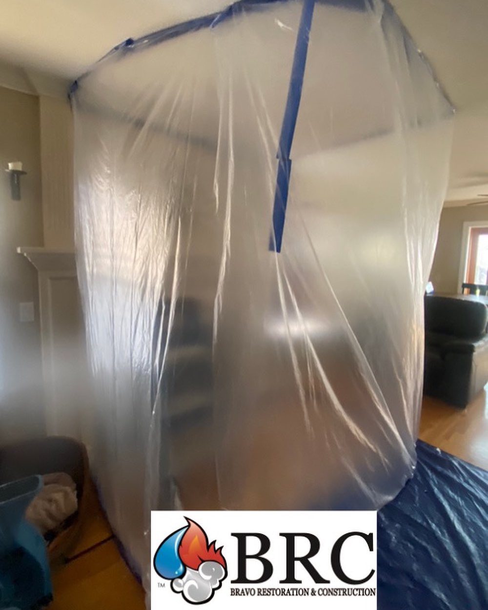 Temporary plastic containment unit set up in a home for construction or restoration, with the logo of bravo restoration & construction visible.