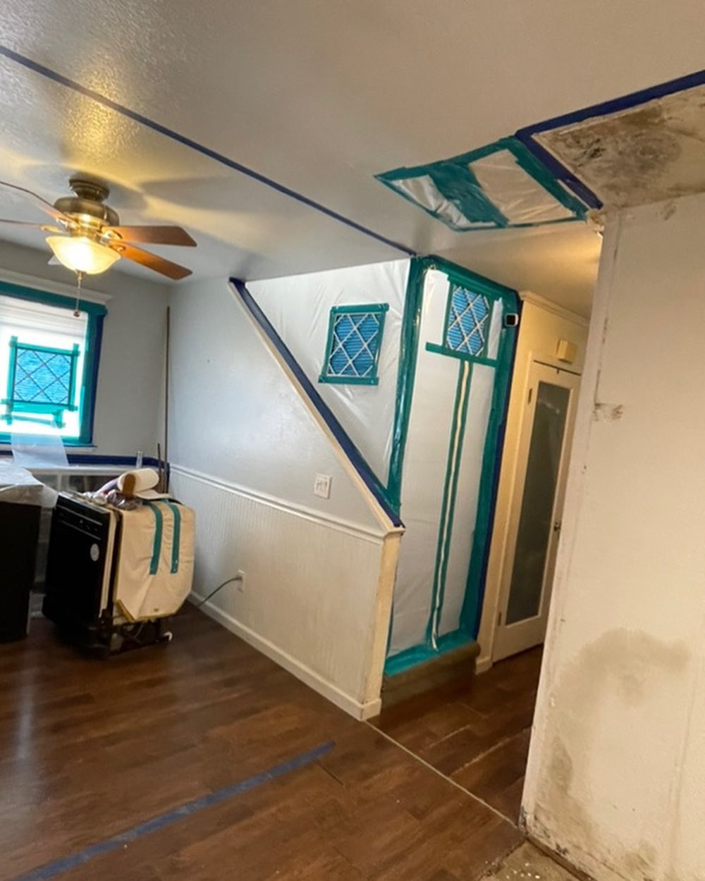 Interior of a house under renovation showing taped edges and unpainted walls, with a fan on the ceiling and a cart in the corner.