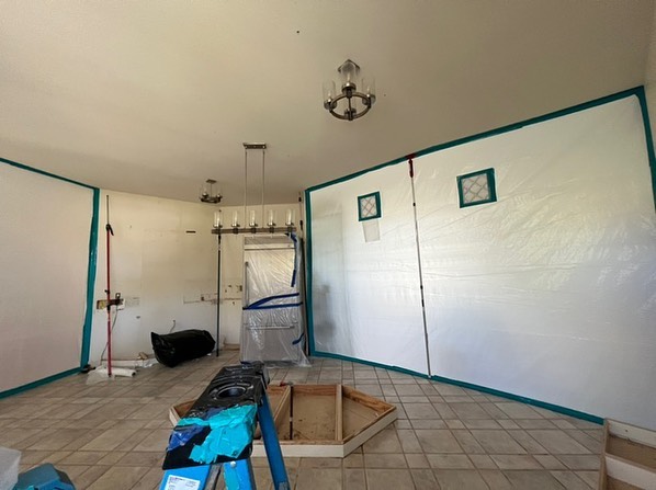 Interior of a room under renovation with protective plastic sheets covering walls and a partially exposed floor.